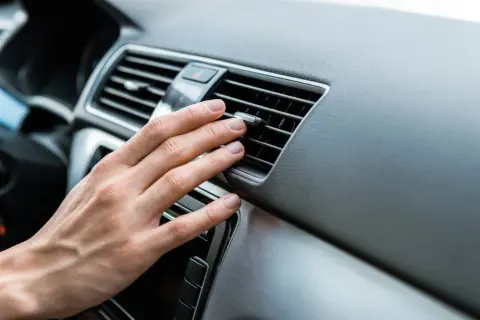 Hand prüft Lüftungsschlitze im Auto. Keine kühle Luft, wahrscheinlich ist der Klimakompressor defekt.