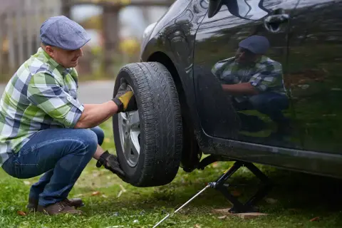Mann wechselt Reifen mit Reifendrucksensor. Er kniet neben dem Auto, das auf einem Wagenheber steht.