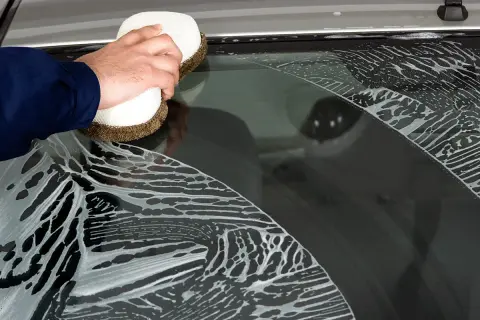 Hand reinigt mit Schwamm und Schaum die Autoscheiben.