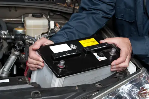 Hände halten eine Autobatterie, um sie aus dem Motorraum zu entfernen. Das **batterie abklemmen** ist ein wichtiger Schritt bei der Wartung.