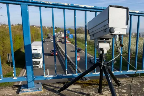Ein Monocam Blitzer auf einem Stativ überwacht den Verkehr auf einer Autobahn. Autos und Lastwagen fahren auf der mehrspurigen Straße.
