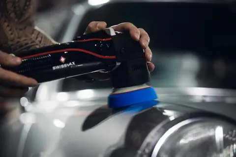 Detailaufnahme: Hand mit Poliermaschine poliert Auto. Glänzender Lack entsteht beim auto selber polieren.