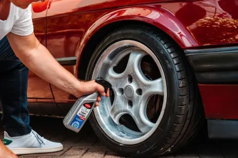Mann sprüht Felgenreiniger auf ein glänzendes Rad eines roten Autos. Die Felgen reinigen wird so zum Kinderspiel.