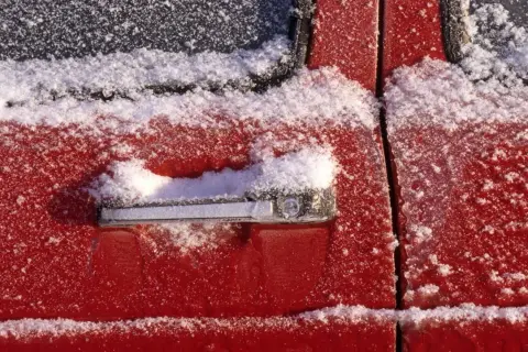 Roter Autolack mit Schnee bedeckt. Wichtig: auto gummi pflegen winter, damit Türen nicht festfrieren.