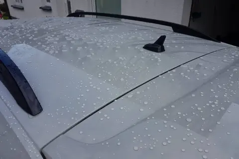 Wassertropfen perlen auf dem Dach eines Autos ab. Ein autoversiegelung test zeigt die wasserabweisende Wirkung.