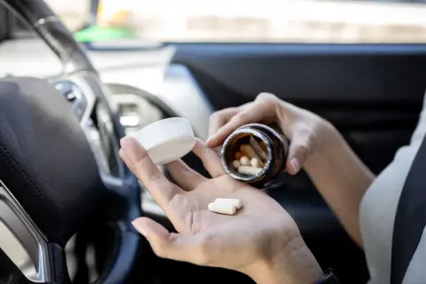 Frau nimmt Ibuprofen im Auto ein. Vorsicht beim Autofahren nach Medikamenteneinnahme.