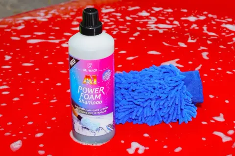 Flasche "A1 Power Foam Shampoo" und blauer Waschhandschuh auf rotem, seifigem Autolack. So gelingt das auto waschen ohne autoshampoo.