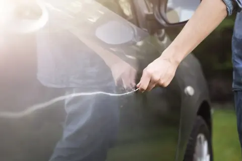 Hand mit Schlüssel verursacht Mikrokratzer am Auto. Die Sonne reflektiert auf dem dunklen Lack.