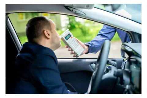 Polizist führt Atemalkoholtest durch. Mann im Auto bläst in Gerät, um die Promillegrenze beim Autofahren zu prüfen.