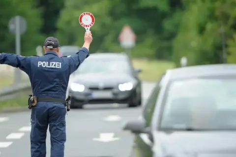 Polizist regelt den Verkehr bei einer allgemeinen Verkehrskontrolle. Er hält ein Stoppschild hoch und winkt Autos weiter.