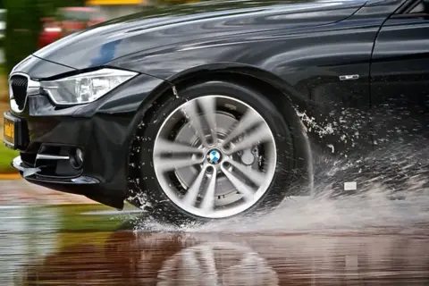 Schwarzer BMW fährt durch Wasserpfützen, was auf einen Uniroyal RainSport 5 Test hindeutet.