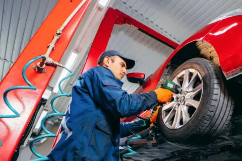 Mechaniker wechselt Reifen am roten Auto. Die Frage "wie lange dauert reifenwechsel" wird hier beantwortet: schnell und effizient.