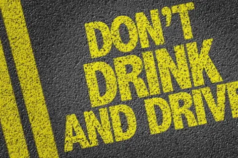 Gelbe Schrift auf Asphalt: "DON'T DRINK AND DRIVE". Informiert über die Promillegrenze Italien.