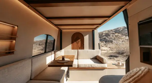 Gemütlicher wohnmobil innen mit Sitzbank, Tisch und Holztür. Blick auf Wüstenlandschaft.