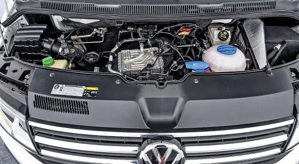 VW T6 150 PS Motorraum mit sichtbaren Leitungen und Kühlmittelbehälter. Mögliche Probleme am Motor sind hier zu sehen.