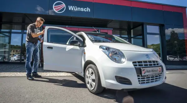 Mann prüft einen weißen Suzuki Alto vor dem Autohaus Wunsch. Mögliche Suzuki Alto Probleme werden hier behoben.