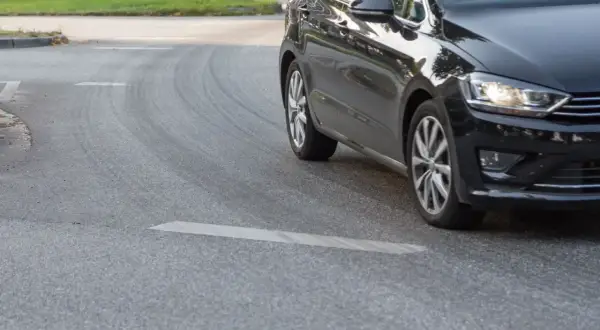 Schwarzes Auto fährt eine Kurve, die Reifen quietschen beim Beschleunigen.