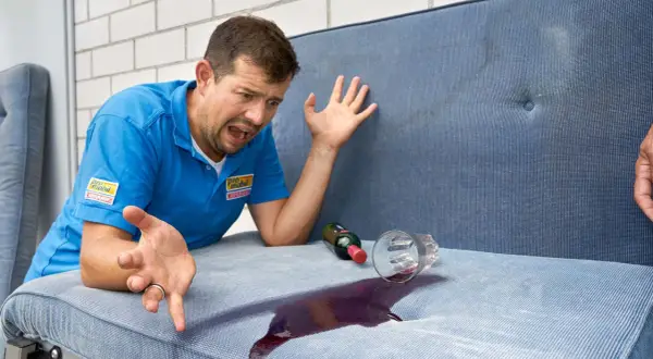 Mann mit verzweifeltem Gesichtsausdruck, der versucht, Rotwein auf einem Wohnwagenpolster zu reinigen.