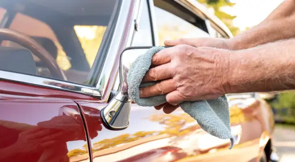 Hände polieren den roten Oldtimer mit einem Mikrofasertuch. So kann das Auto wachsen ohne polieren, für einen glänzenden Auftritt.