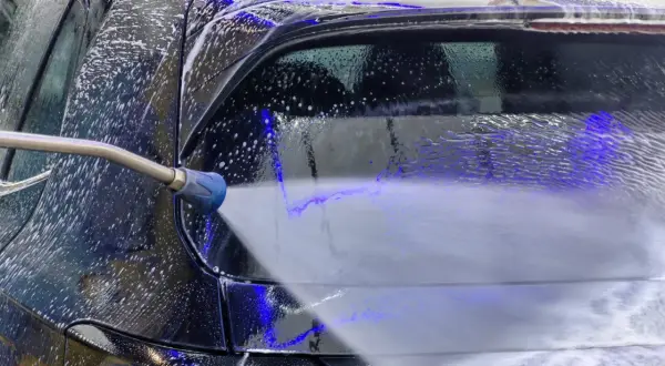 Ein Hochdruckreiniger spritzt Schaum auf ein schwarzes Auto. Die richtige auto waschen reihenfolge sorgt für Glanz.
