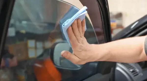 Hand wischt mit blauem Tuch die Windschutzscheibe innen reinigen streifenfrei.