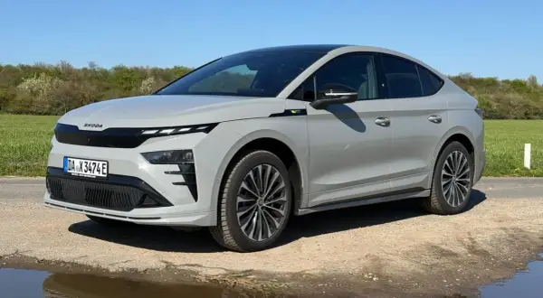 Grauer Skoda Enyaq Coupé auf staubiger Straße, umgeben von grünen Feldern. Manche Fahrer berichten von Skoda Enyaq Problemen, aber dieses Modell scheint unbeeindruckt.