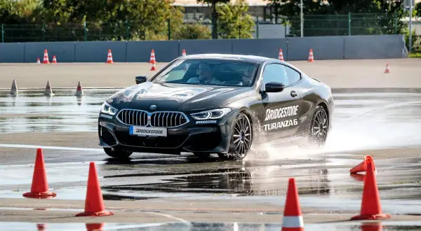 BMW fährt auf nasser Strecke, Wasser spritzt. Bridgestone Turanza 6 Test auf dem Prüfstand.