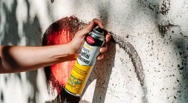Hand hält Sprühdose mit Graffiti-Entferner. Ideal, um Graffiti von Wänden zu entfernen, fast wie felgenreiniger selber machen.