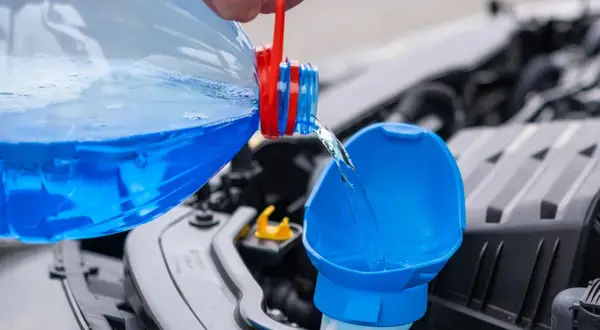 Blauer Scheibenreiniger wird aus einer Flasche in den Einfüllstutzen gegossen. Perfekt für das Scheibenwischwasser Sommer selber machen.