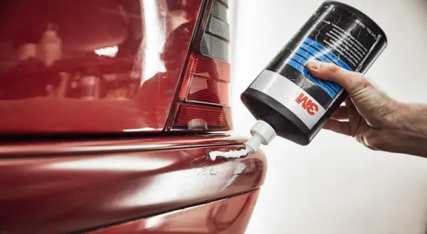 Hand drückt 3M-Paste auf zerkratzten roten Autolack. So lassen sich auto kratzer entfernen und der Glanz wiederherstellen.