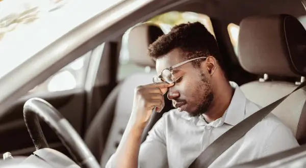 Mann im Auto mit Kopfschmerzen, fragt sich, darf man mit Antidepressiva Autofahren?