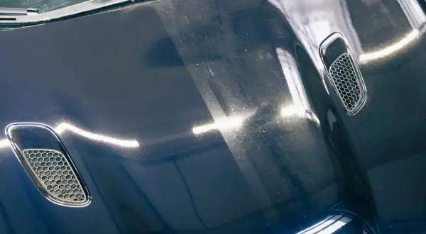 Dunkelblaue Motorhaube mit Lüftungsgittern, zeigt deutliche Swirls und Kratzer. Die Kosten für Motorhaube polieren sind hier sichtbar.