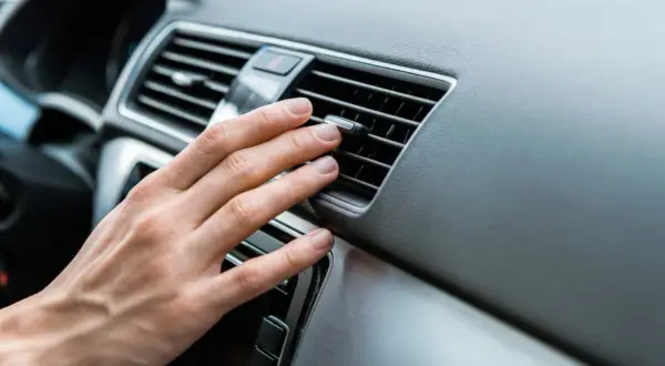 Hand prüft Lüftungsschlitze im Auto. Keine kühle Luft, wahrscheinlich ist der Klimakompressor defekt.