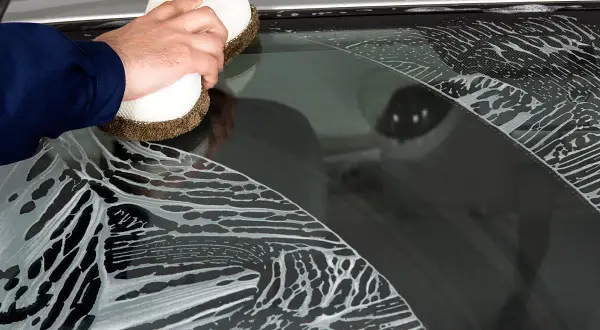 Hand reinigt mit Schwamm und Schaum die Autoscheiben.