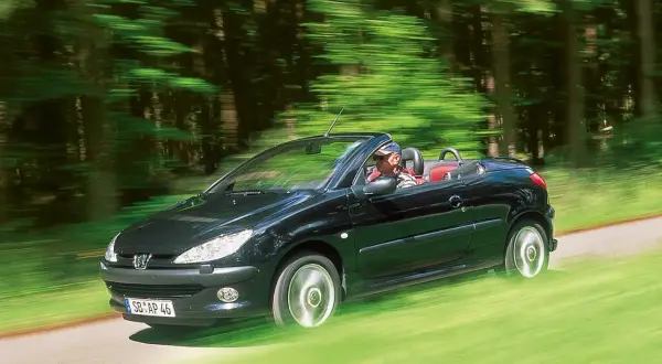 Schwarzer Peugeot 206 CC fährt offen durch grünen Wald. Bekannte peugeot 206 cc schwachstellen sind hier nicht sichtbar.