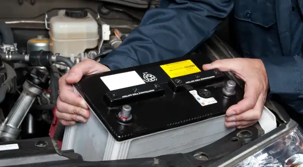 Hände halten eine Autobatterie, um sie aus dem Motorraum zu entfernen. Das **batterie abklemmen** ist ein wichtiger Schritt bei der Wartung.