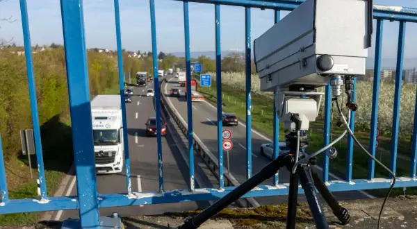 Ein Monocam Blitzer auf einem Stativ überwacht den Verkehr auf einer Autobahn. Autos und Lastwagen fahren auf der mehrspurigen Straße.
