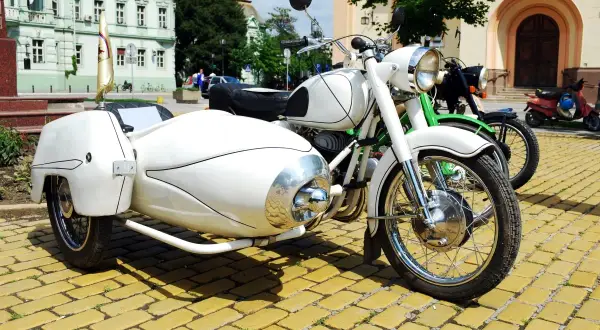 Weiße Motorräder mit Beiwagen und Roller stehen auf einem gelben Kopfsteinpflaster. Ein Helm liegt auf dem Roller, um die Strafe für Fahren ohne Helm zu vermeiden.