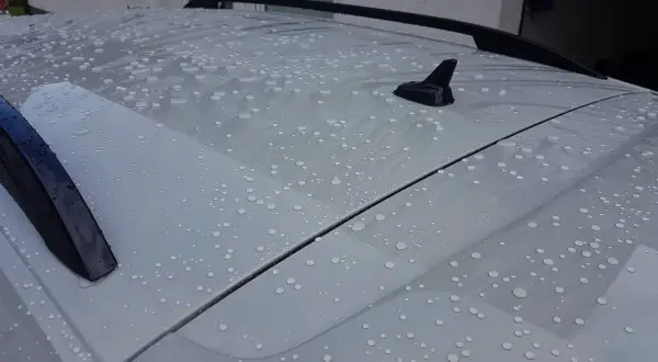 Wassertropfen perlen auf dem Dach eines Autos ab. Ein autoversiegelung test zeigt die wasserabweisende Wirkung.
