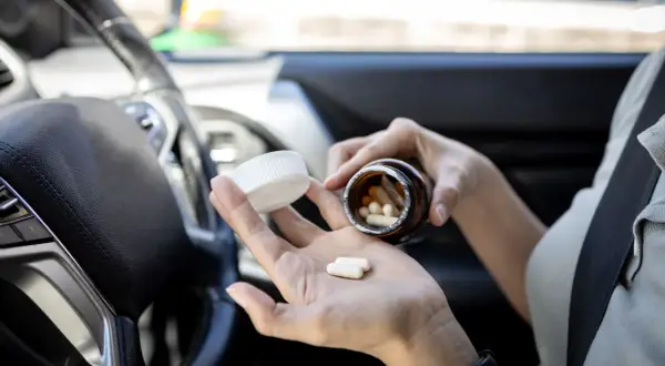 Frau nimmt Ibuprofen im Auto ein. Vorsicht beim Autofahren nach Medikamenteneinnahme.