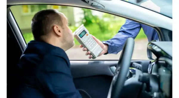 Polizist führt Atemalkoholtest durch. Mann im Auto bläst in Gerät, um die Promillegrenze beim Autofahren zu prüfen.