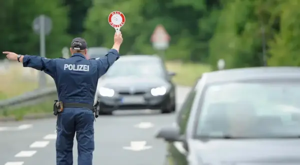 Polizist regelt den Verkehr bei einer allgemeinen Verkehrskontrolle. Er hält ein Stoppschild hoch und winkt Autos weiter.