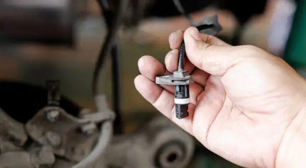 Hand hält ABS-Sensor. Defekter ABS-Sensor Symptome können durch Austausch behoben werden.