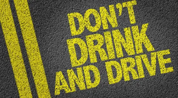 Gelbe Schrift auf Asphalt: "DON'T DRINK AND DRIVE". Informiert über die Promillegrenze Italien.