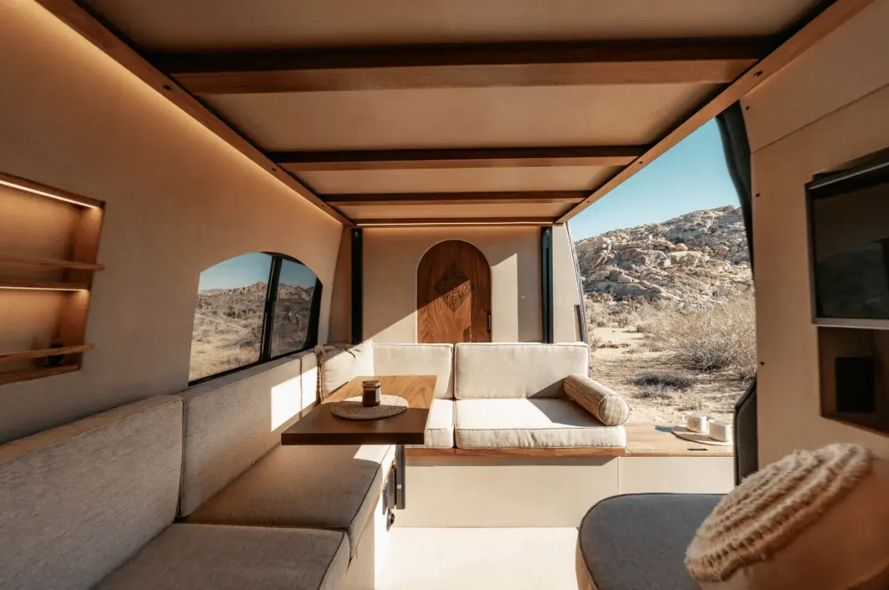 Gemütlicher wohnmobil innen mit Sitzbank, Tisch und Holztür. Blick auf Wüstenlandschaft.
