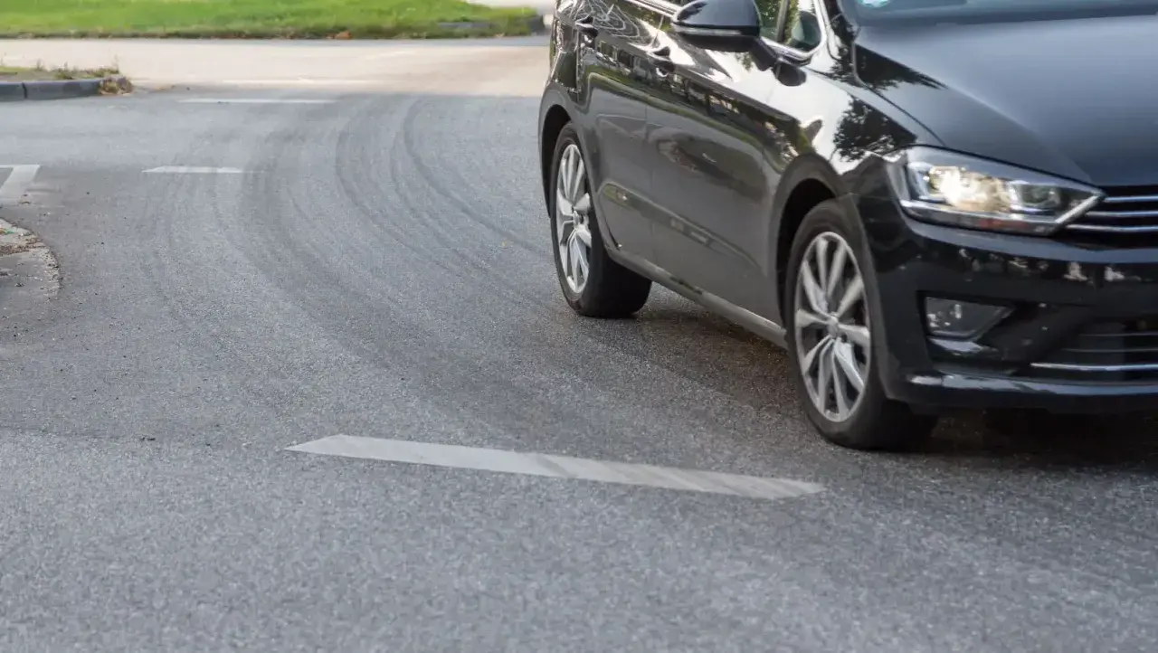 Schwarzes Auto fährt eine Kurve, die Reifen quietschen beim Beschleunigen.