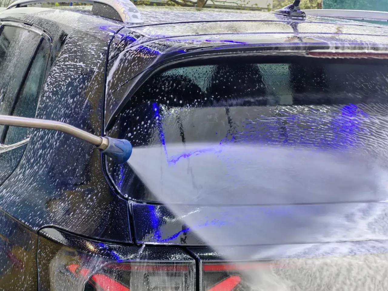 Ein Hochdruckreiniger spritzt Schaum auf ein schwarzes Auto. Die richtige auto waschen reihenfolge sorgt für Glanz.