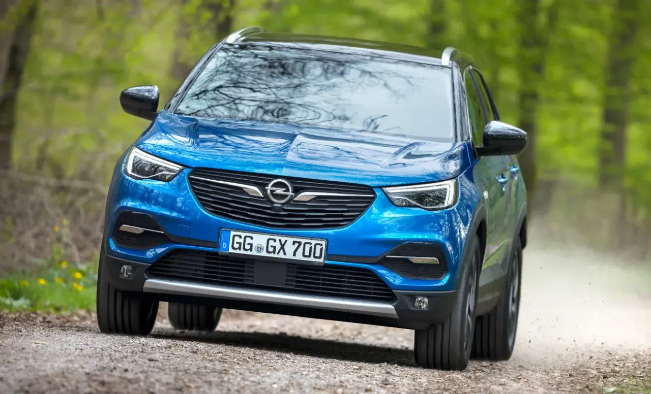 Blauer Opel Grandland X fährt auf einem Feldweg durch grünen Wald.