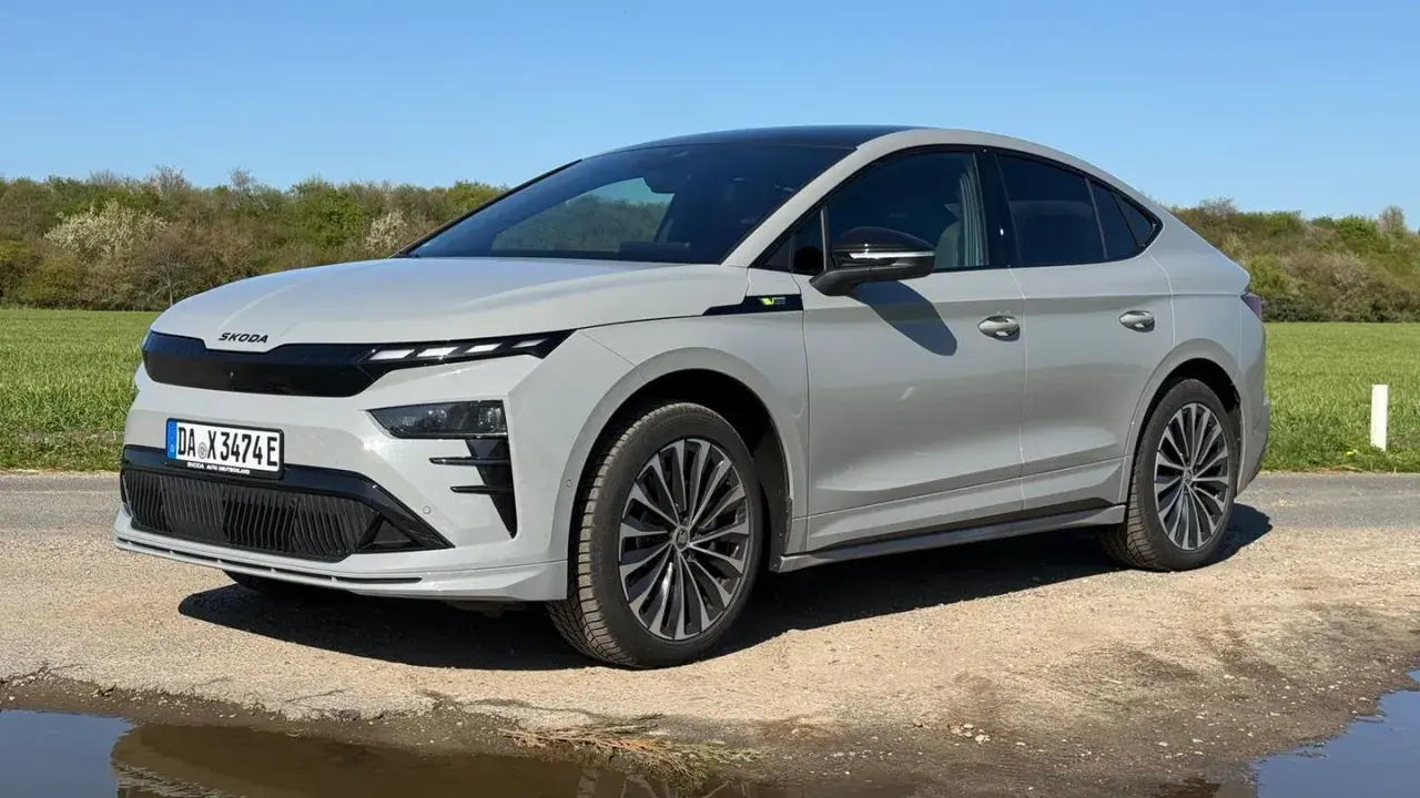Grauer Skoda Enyaq Coupé auf staubiger Straße, umgeben von grünen Feldern. Manche Fahrer berichten von Skoda Enyaq Problemen, aber dieses Modell scheint unbeeindruckt.