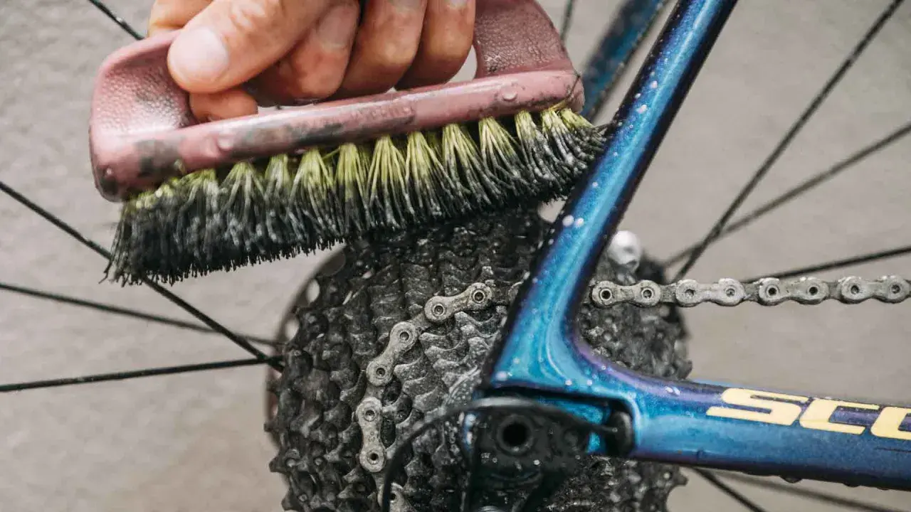 Mit Hausmitteln die Fahrradkette reinigen: Eine Bürste schrubbt die Kette und Kassette des glänzenden blauen Fahrradrahmens.